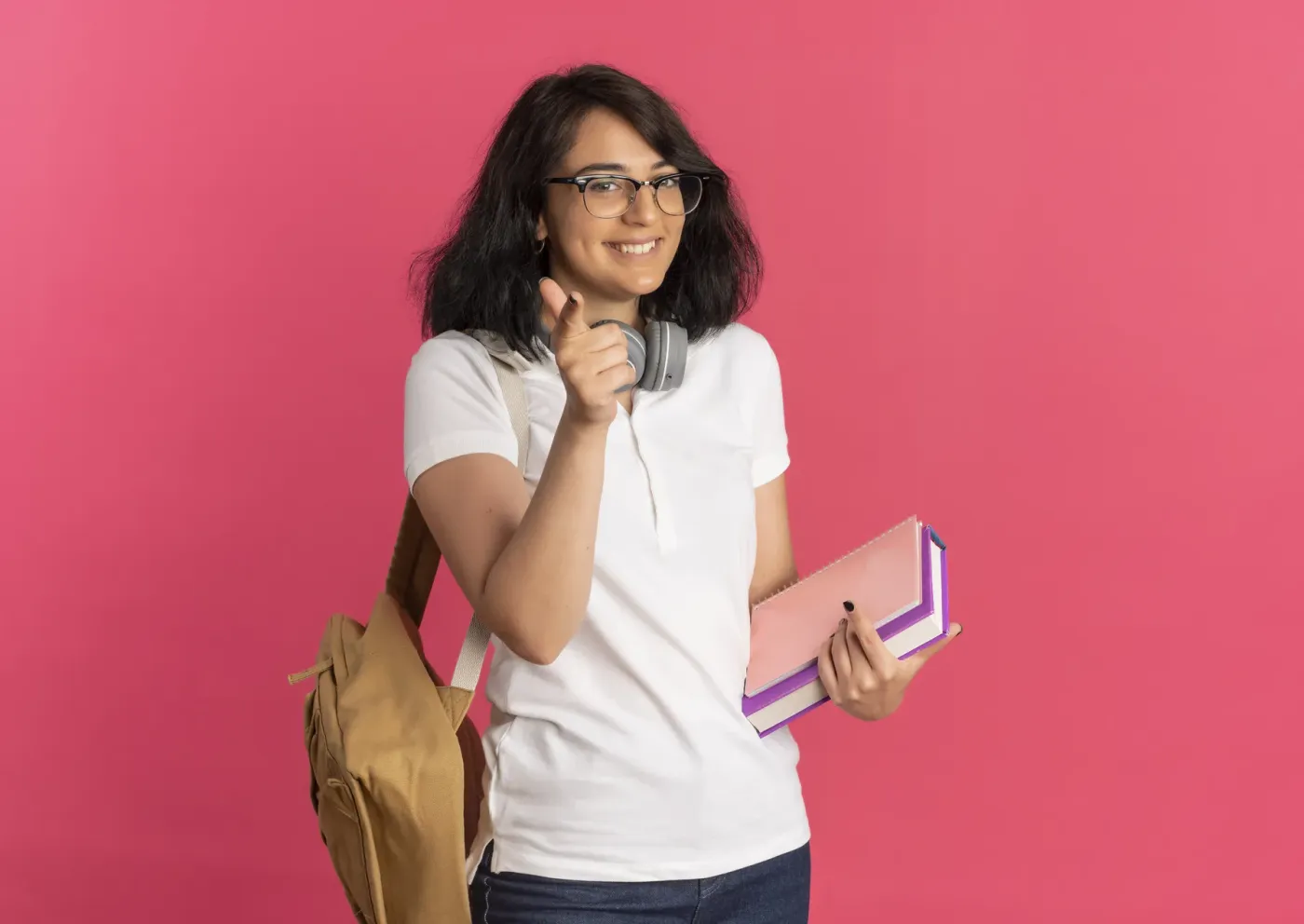 A smiling student with headphones, a backpack and books